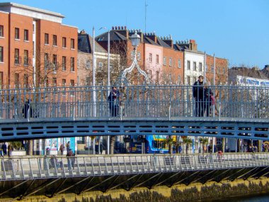 Dublin, İrlanda - Şubat 2018: Dublin 'in merkezindeki Liffey Nehri üzerinden Halfpenny Köprüsü' nü geçen insanlar