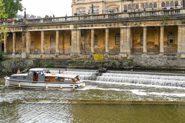 Bath, İngiltere - Ağustos 2021: Bath 'ın merkezindeki Pulteney Weir' da dönen motorlu tekne, yukarıdaki balkondan aşağı bakan ziyaretçiler