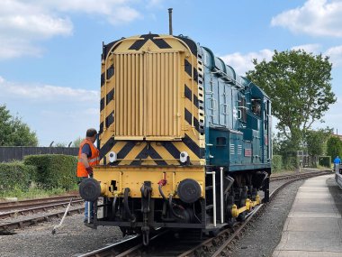 Didcot, Oxford, İngiltere - Haziran 2021: Didcot Buhar Demiryolu Merkezi 'ndeki dizel şönlü lokomotifin önünde otostop çeken demiryolu işçisi