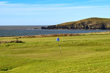 Sahildeki bir golf sahasının yeşilindeki delikte bayrak var. Kimse yok..