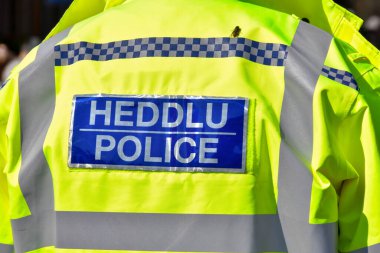 Cardiff, Wales - Mart 2022: Cardiff şehir merkezinde görevli bir polis memurunun ceketinin üzerindeki çift dilli tabelanın arkası