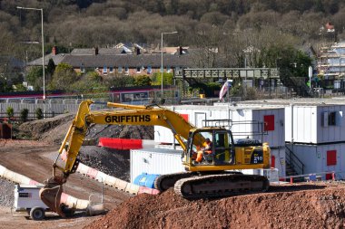 Taffs Well, Wales - Mart 2022: Büyük bir çakıl yığını üzerinde büyük bir mekanik kazıcı olarak çalışan kişi.