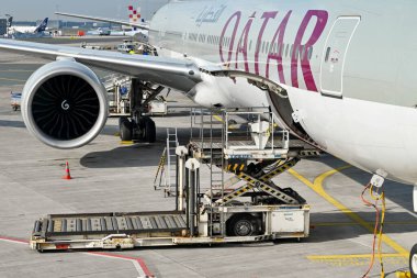Frankfurt, Almanya - Nisan 2022: Katar Havayolları Boeing 777 jetinin açık yük ambarının yanında hidrolik hava yükü yükleyicisi.
