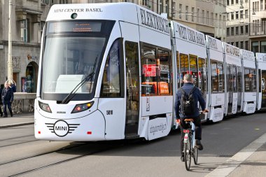 Basel, İsviçre - Nisan 2022: Bisikletçi şehrin modern tramvaylarından birinin yanından geçiyor. Şehrin geniş bir tramvay ağı var.