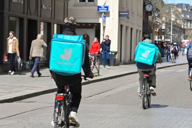 Strasbourg, France - April 2022: Delivery persons with backpacks for Deliveroo riding bicycles on a street in Strasbourg city centre