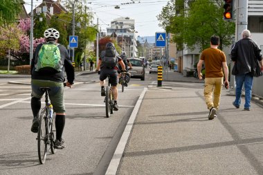 Basel, İsviçre - Nisan 2022: İnsanlar şehir merkezinin varoşlarındaki bir sokakta işten eve bisikletle dönüyorlar