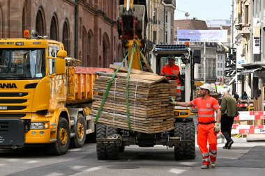 Basel, İsviçre - Nisan 2022: İnşaat işçisi gezici bir mekanik kazıcının yardımıyla şehir merkezindeki bir caddede ağır bir kerestenin taşınmasına yardım ediyor