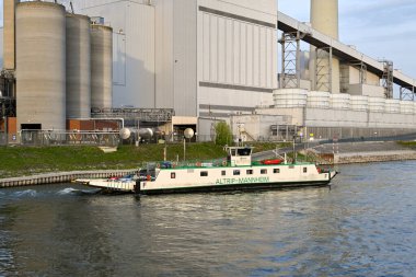 Mannheim, Almanya - Nisan 2022: Ren nehrinin kenarında yer alan büyük enerji santraline araba ve yolcu taşıyan küçük feribot.