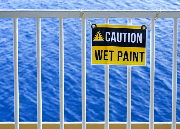 Wet Paint sign on metal railings with the sea in the background. No people.