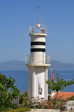 Kusadasi, Türkiye - Haziran 2022: Kuşadası limanındaki Güvercin Adası 'ndaki deniz fenerinin yanından geçen ziyaretçiler.