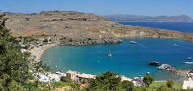 Lindos, Rodos, Yunanistan - Mayıs 2022: Güneş şemsiyeleri ve denizde küçük teknelerle sahilin havadan görünüşü