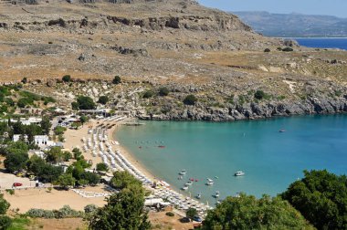 Lindos, Rodos, Yunanistan - Mayıs 2022: Güneş şemsiyeleri ve denizde küçük teknelerle sahilin havadan görünüşü