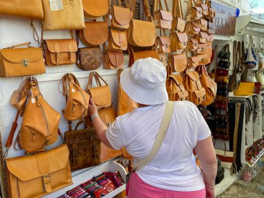 Lindos, Rodos, Yunanistan - Mayıs 2022: Kentin pek çok mağazasından birinde satışta olan deri çantalara bakan kişi