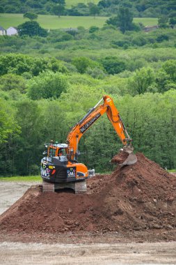 Pontypridd, Wales - July 2022: Mechanical digger working on top of a large mound of soil preparing the ground for a new housing development