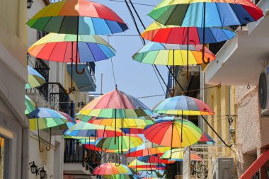 Aegina, Yunanistan - Mayıs 2022: Segina kentinin dar sokaklarından birinin üzerinde asılı renkli şemsiyeler