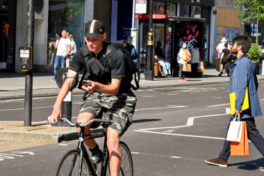 London, UK - June 2022: Person looking down at his mobile phone while riding a biycycle along Oxford Street