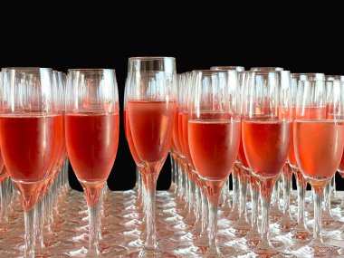 Rows of flute glasses filled with pink champagne against a plain black background. No people.