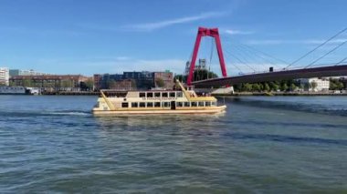 Rotterdam, The Netherlands  August 2022: Tourist river cruise boat sailing under the Willemsbrug suspension bridge, which spans the Nieuwe Maas.