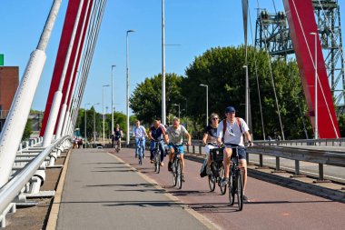 Rotterdam, Netherlands - August 2022: People riding bicycles in the cycle lane over the Willems Bridge in the city centre over the Nieuwe Maas river.