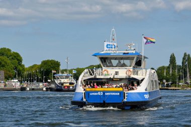 Amsterdam, Netherlands - August 2022: River ferry arriving at the waterfront with a crowd of people on deck