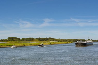 Rotterdam, Netherlands - August 2022: Industrial barge sailing with two small lesiure boats. Contrast concept