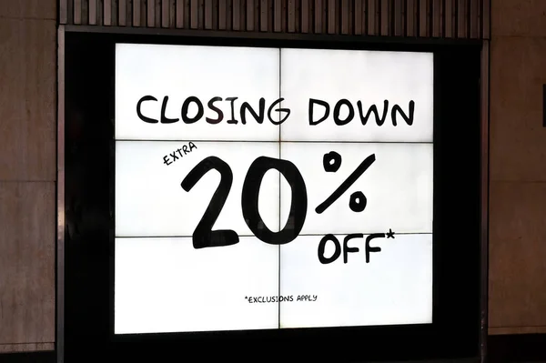 Illuminated sign outside a retail store adverrtising a closing down sale. No people.