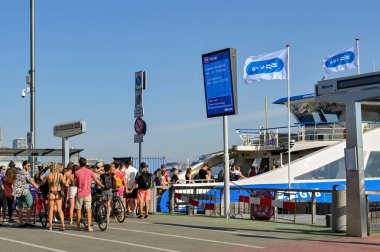 Amsterdam, Netherlands - August 2022: Crowd of people and cyclists catching a river ferry from the city centre