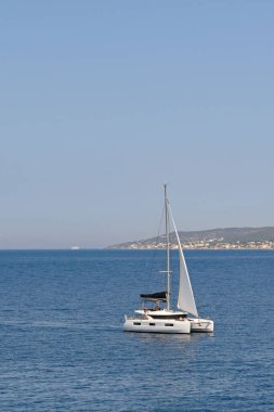 Aegina, Yunanistan - Mayıs 2022: Modern katamaran teknesi Aegina adası açıklarında sakin bir deniz boyunca yavaşça ilerliyor.