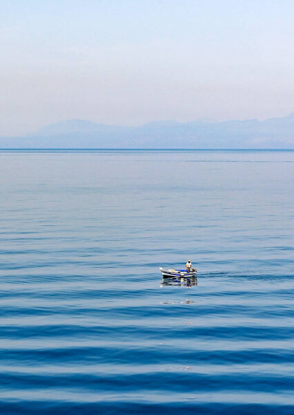 Aegina, Greece, - May 2022: Person standing up in a small fishing boat on a blue sea with wave pattern