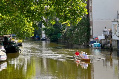 Amsterdam, Hollanda - Ağustos 2022: Olgun kadınlarla birlikte şehir merkezinde bir kanalda egzersiz yapan kayık