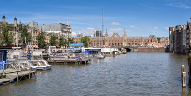 Amsterdam, Hollanda - Ağustos 2022: Şehir merkezindeki iskelelere demirlemiş turistik kanal gezileri. Arka planda şehrin Centraale tren istasyonu var..