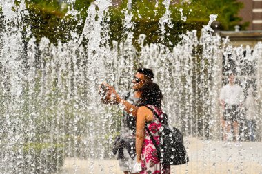 Amsterdam, Hollanda - Ağustos 2022: Halk bahçesindeki bir fıskiyenin ortasında durarak selfie çeken iki kişi