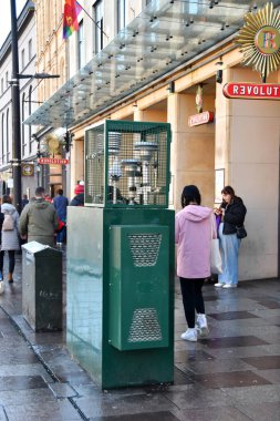 Cardiff, Wales - Ekim 2022: Cardiff şehir merkezindeki bir caddedeki şehir kirliliğini ölçmek için bir hava kalite izleme istasyonunun önünden geçen insanlar