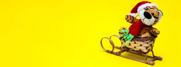 A toy New Year tiger riding on a sleigh. Banner. The tiger is a symbol of the new year 2022. Yellow background.