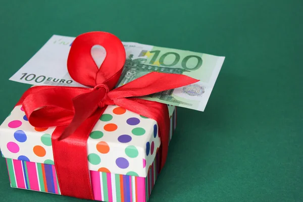 100-Euro-Schein auf einem Geschenkkarton mit roter Schleife. Grüner Hintergrund. lizenzfreie Stockbilder