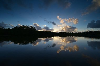 Florida Everglades Ulusal Parkı 'ndaki Paurotis Gölü' nün sakin sularını yansıtan renkli günbatımı bulutları.