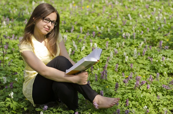 Ritratto di bella ragazza con libro e occhiali nei fronti primaverili — Foto Stock