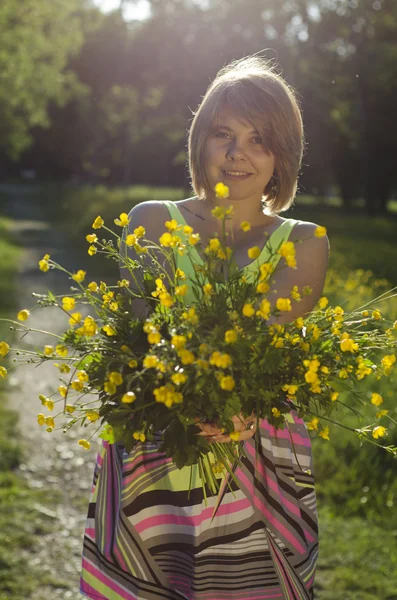 Piękna dziewczyna uśmiechający się trzyma kwiat (Jaskier) w zachód słońca — Zdjęcie stockowe
