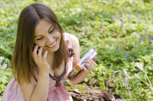 Beautiful smiling girl with book is speaking on phone — Stock Photo, Image