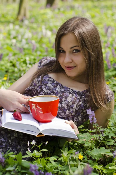 Sorridente bella ragazza è in possesso di tazza rossa e libro — Foto Stock