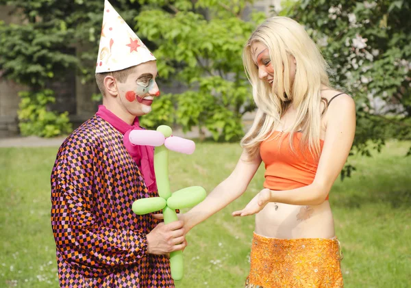 Portræt af en smilende mand klædt som en klovn præsenteret en ballon til en glad pige med sommerfugl makeup - Stock-foto