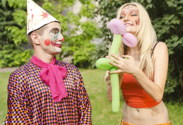 Portrait of a smiling man dressed like a clown presented a balloon to a happy girl with butterfly makeup — Stock Photo, Image