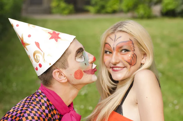 Retrato del hombre vestido como un payaso tratando de besar a una chica con maquillaje de mariposa Imagen de archivo