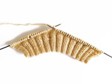 knitting on knitting needles from beige wool on a white background