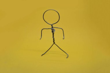 Kablodan yapılmış metal adam sarı arka planda duruyor.