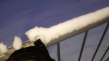 A man removes snow from a handrail with a glove