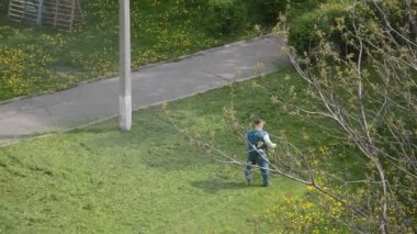 Yaşlı bir adam bahçede bir benzin makası biçiyor.