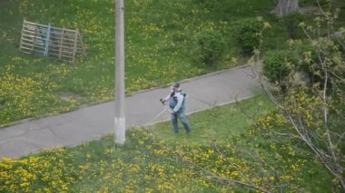 Yaşlı bir adam bahçede bir benzin makası biçiyor.