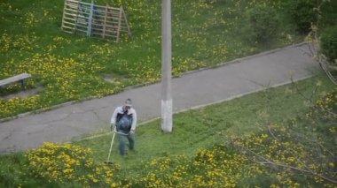 Yaşlı bir adam bahçede bir benzin makası biçiyor.