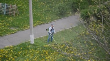 Yaşlı bir adam bahçede bir benzin makası biçiyor.